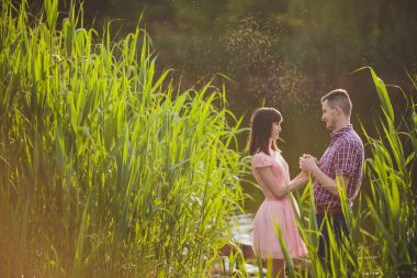 Göldeki aşıklar. Bu genç adam gün batımında gitar çalarken genç çift parkta, suyun kenarında oturuyor..