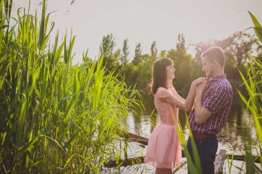 Göldeki aşıklar. Bu genç adam gün batımında gitar çalarken genç çift parkta, suyun kenarında oturuyor..
