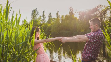 Göldeki aşıklar. Bu genç adam gün batımında gitar çalarken genç çift parkta, suyun kenarında oturuyor..