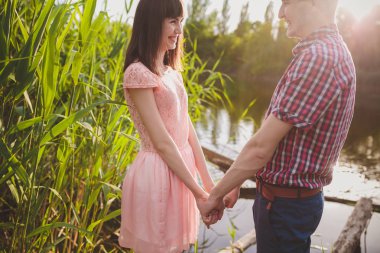 Göldeki aşıklar. Bu genç adam gün batımında gitar çalarken genç çift parkta, suyun kenarında oturuyor..