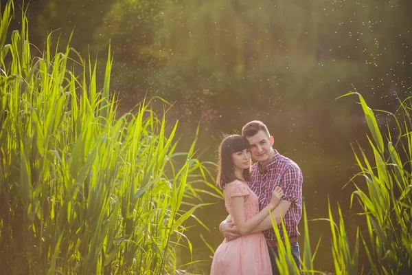 Göldeki aşıklar. Bu genç adam gün batımında gitar çalarken genç çift parkta, suyun kenarında oturuyor..