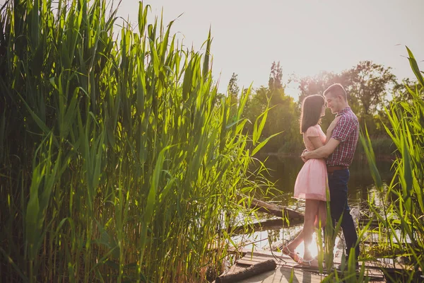 Verliebte in einem See. Junges verliebtes Paar sitzt auf dem Parkgelände am Wasser, während dieser junge Mann im Sonnenuntergang Gitarre spielt. — Stockfoto