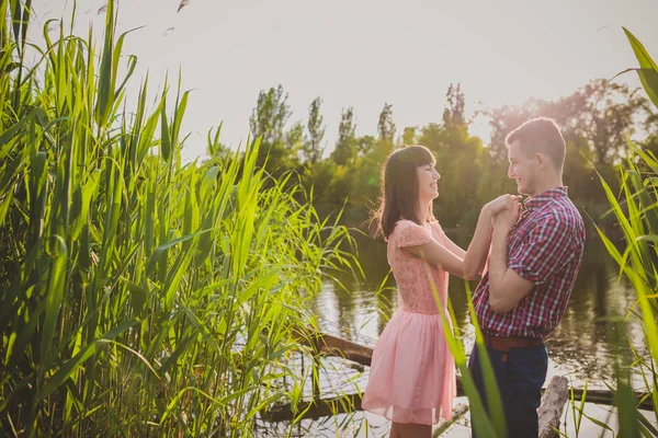 Amantes en un lago. Pareja joven enamorada sentada en el suelo del parque cerca del agua mientras estos jóvenes tocan la guitarra al atardecer. — Foto de Stock