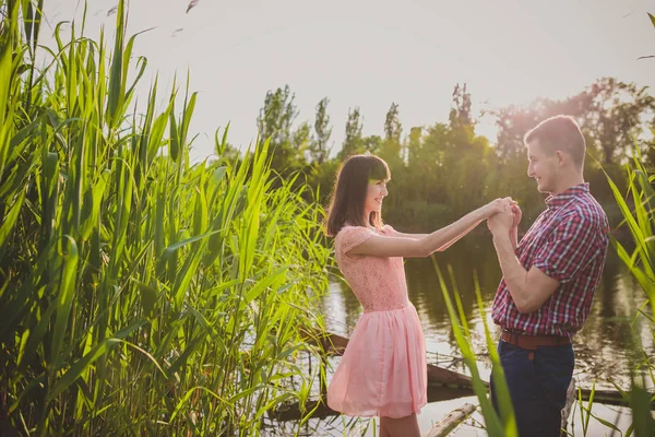 Amantes en un lago. Pareja joven enamorada sentada en el suelo del parque cerca del agua mientras estos jóvenes tocan la guitarra al atardecer. — Foto de Stock