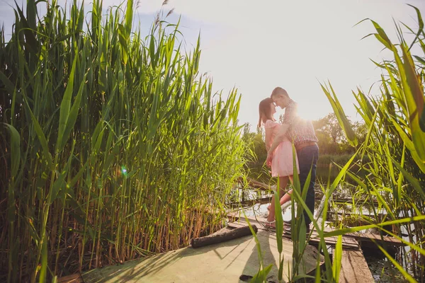 Göldeki aşıklar. Bu genç adam gün batımında gitar çalarken genç çift parkta, suyun kenarında oturuyor..