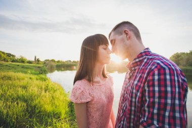 Göldeki aşıklar. Bu genç adam gün batımında gitar çalarken genç çift parkta, suyun kenarında oturuyor..