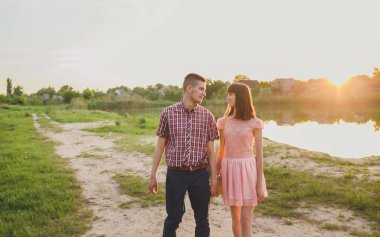 Göldeki aşıklar. Bu genç adam gün batımında gitar çalarken genç çift parkta, suyun kenarında oturuyor..