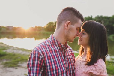 Göldeki aşıklar. Bu genç adam gün batımında gitar çalarken genç çift parkta, suyun kenarında oturuyor..