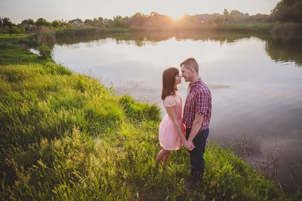 Göldeki aşıklar. Bu genç adam gün batımında gitar çalarken genç çift parkta, suyun kenarında oturuyor..