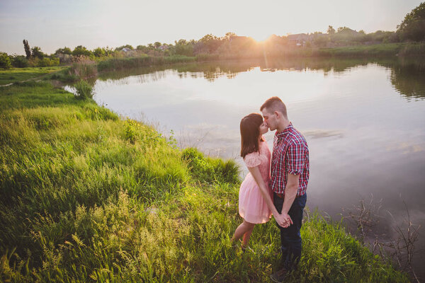 Lovers in a lake. Young couple in love sitting on the park ground near the water while these young man playing guitar in sunset time.