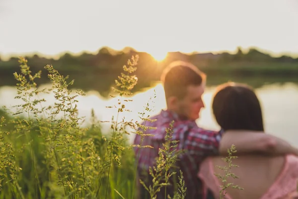 Göldeki aşıklar. Bu genç adam gün batımında gitar çalarken genç çift parkta, suyun kenarında oturuyor..
