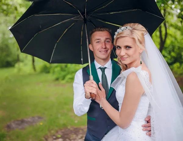 Beautiful bride and groom walking under umbrella at park. Bride with red hair. — Stock Photo, Image