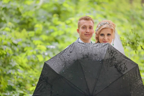 Beautiful bride and groom walking under umbrella at park. Bride with red hair. — Stock Photo, Image
