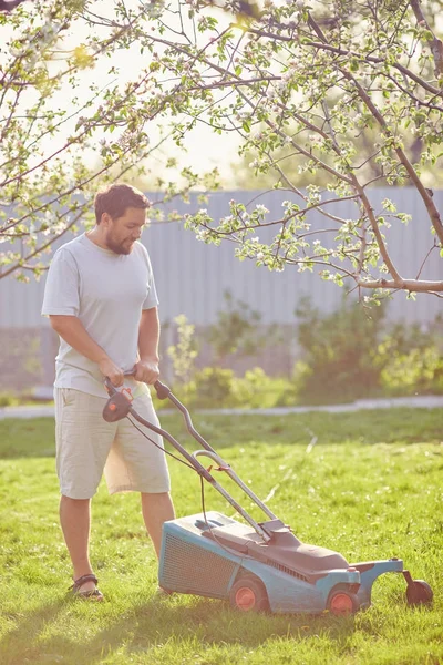 Låg vinkel syn på ung man klipper gräsmattan — Stockfoto