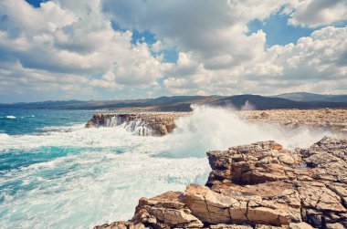 Big waves break about the Rocky Peninsula of Cape Lara in southe clipart