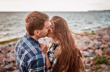 Göldeki aşıklar. Bu genç adam gün batımında gitar çalarken genç çift parkta, suyun kenarında oturuyor..