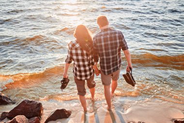 Kareli gömlekli çift gölün kıyısında durur, öpüşür ve gün batımıyla tanışır.