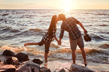 Kareli gömlekli çift gölün kıyısında durur, öpüşür ve gün batımıyla tanışır.