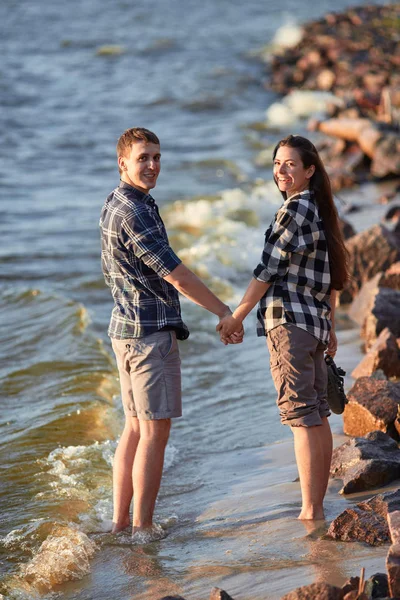 Young couple in plaid shirts walking along the shore of the lake — Stock Photo, Image