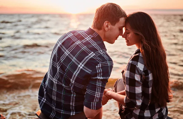 Pareja amorosa en camisas a cuadros se encuentra en la orilla del lago, besos y se encuentra con la puesta de sol — Foto de Stock