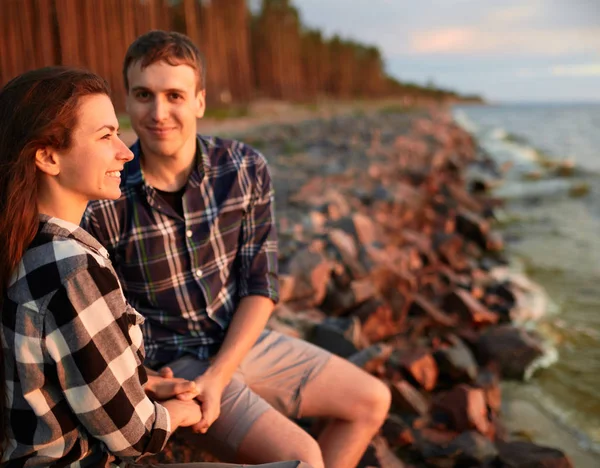 Milující pár v kostkovaných košilích stojí na břehu jezera, polibky a potkává západ slunce — Stock fotografie