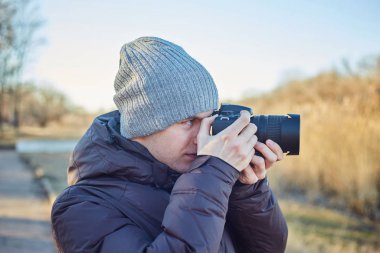 Şapkalı bir fotoğrafçı, kış parkında fotoğraf çekiyor.