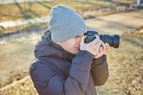 Fotograf mit Hut, macht ein Foto mit seiner Kamera im Winterpark — Stockfoto