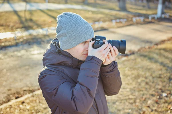 Fotógrafo en un sombrero, hace una foto en su cámara en el parque de invierno — Foto de Stock