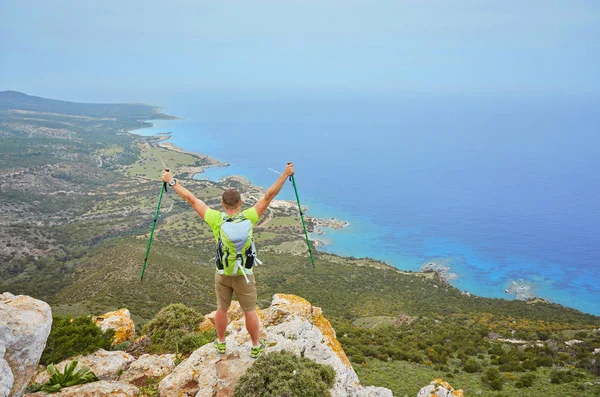 A young man on top of a mountain raised his hands up holding trekking poles. — Stock Photo, Image