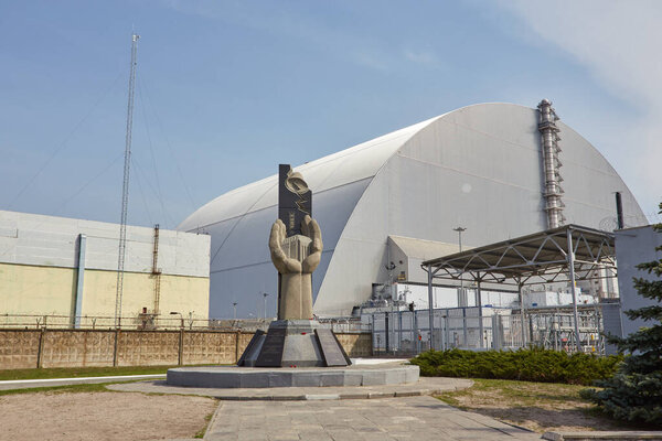 PRIPYAT, UKRAINE - April 25 2019: Monument to the Chernobyl Liquidators and fourth reactor without enclosing sarcophagus. Chornobyl Nuclear Power Plant - ChNPP