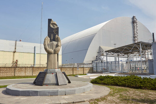ПРИПЯТ, УКРАИНА - 25 апреля 2019 года: Памятник ликвидаторам Чернобыля и четвертый реактор без прикрепления саркофага. Чернобыльская АЭС - ЧАЭС
