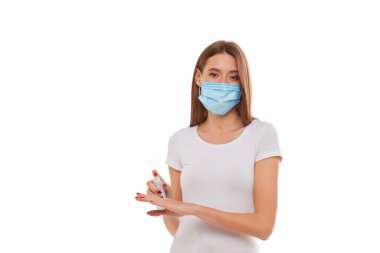 Avrupalı kız tıp maskesi ellerine antiviral, antiseptik bir el spreyi sürüyor. Salgın temalı kavramsal fotoğraf. Beyaz bir arkaplanda izole edilmiş.