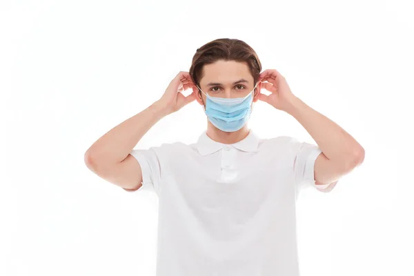 Un hombre con una camiseta blanca de apariencia europea se pone una máscara médica . — Foto de Stock