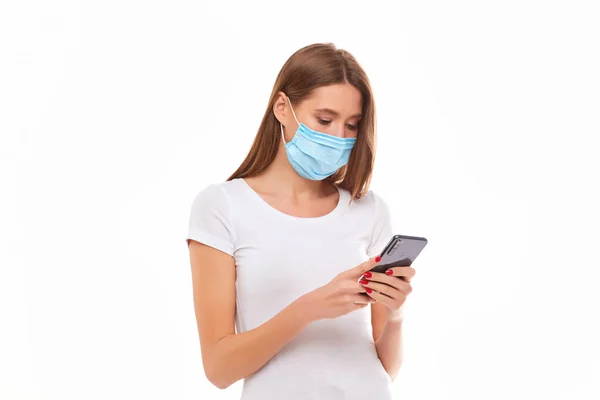 Chica Europea en una máscara utiliza un teléfono. Foto conceptual sobre el tema de la epidemia . — Foto de Stock