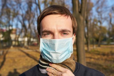 Sokakta yüzüne tıbbi maske takan ceketli bir adam.