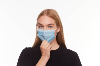 Yüzünde tıbbi maske tutan bir kızın stüdyo portresi. Virüs koruması. Beyaz arkaplanda izole edilmiş, kapat.