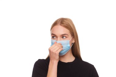 Yüzünde tıbbi maske tutan bir kızın stüdyo portresi. Virüs koruması. Beyaz arkaplanda izole edilmiş, kapat.