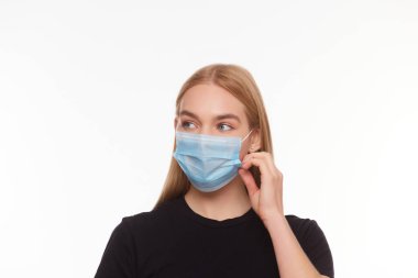 Yüzünde tıbbi maske tutan bir kızın stüdyo portresi. Virüs koruması. Beyaz arkaplanda izole edilmiş, kapat.
