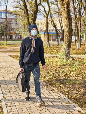 Elinde evrak çantası olan şapkalı genç bir adam tıbbi maskeyle işe gitmek için caddede yürüyor. Şehirde karantina, bir salgın var..