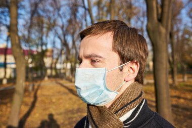 Tıbbi maskeli genç adamın portresi şehir caddesinde duruyor. Dışarıdaki kalabalığın içinde virüsten koruyucu maske takan adam. Coronavirüs salgınından sağIık ve güvenlik kavramı.