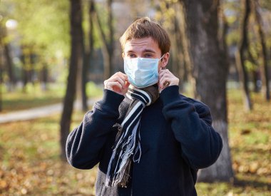 Sokakta yüzüne tıbbi maske takan ceketli bir adam.