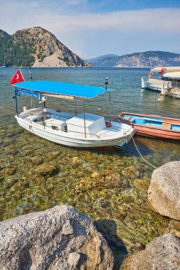 Türkiye 'nin Mugla, Turunc kentindeki tepenin tepesinde Ege Denizi' ndeki mavi lagün, arka planda plaj ve Türk bayrağı bulunan küçük tekneler.