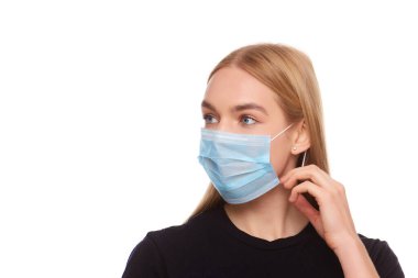 Sarışın, tıbbi maske takan genç bir kadın elleriyle düzeltiyor izole edilmiş beyaz arka planı.