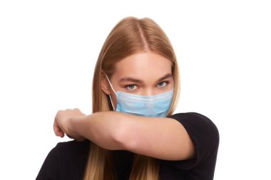 Tıbbi steril maske takan, hapşıran ve dirseğiyle üstünü örten genç bir kadının portresi. Coronavirus 'tan korunan bir kıza yakın çekim. Karantina Evde Kalma Konsepti