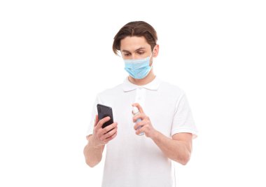 European man in a mask disinfects the phone. Conceptual photo on the theme of the covid-2019 pandemic. Isolated on white background clipart