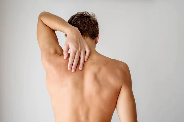 Genç ve formda bir adam çıplak kaslı sırtla ayakta duruyor ve eliyle omzuna dokunuyor. Sırt ağrısı ve omurga sorunları kavramı.