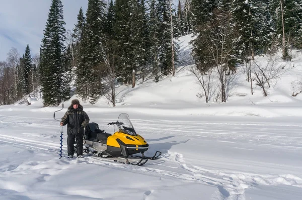 Fiskaren står med is skruvar nära snöskotern — Stockfoto