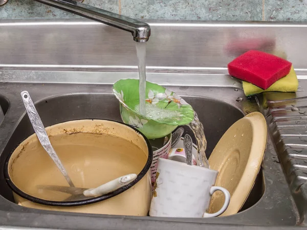 Dirty dishes in a sink under running water — Stock Photo, Image