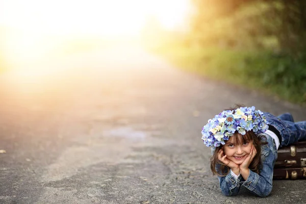 道路上の古いスーツケースと花輪の少女 — ストック写真