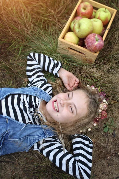Γελώντας νεαρή κοπέλα βρίσκεται στο γρασίδι με ένα καλάθι με μήλα — Φωτογραφία Αρχείου
